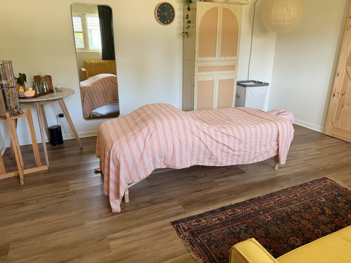 The treatment room, table made up, with a full-length mirror and cane-front cabinet