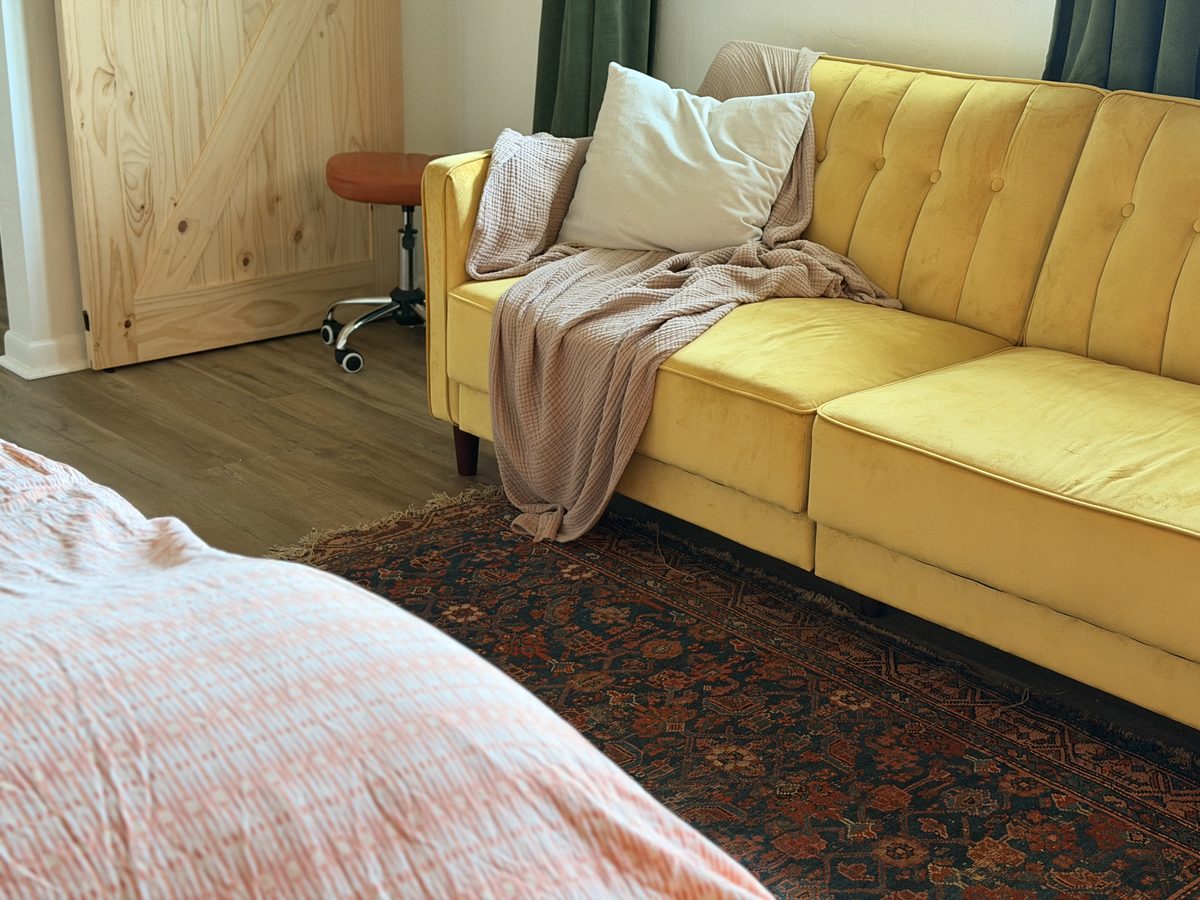 The mustard velvet sofa with a linen throw, over a patterned Persian rug